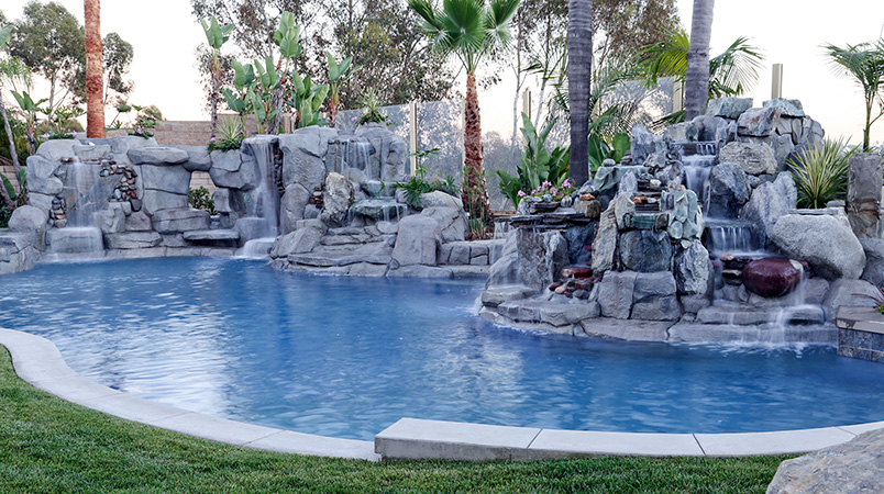 Swan Pools created this custom swimming pool interwined with the custom cottage in the wooded hills of Newport Beach, California.  Custom freestanding swimming pool and raised spa myander between the residence and pool house connected by a stone veneered, raised footbridge spanning the swimming pool and private cove.  Stone coping finishes the swimming pool well including, Caribbean Blue quartz plaster, led lighting, remote systems, and raised spa veneered in stone with custom width coping perfect for cool beachside evening entertaining. 